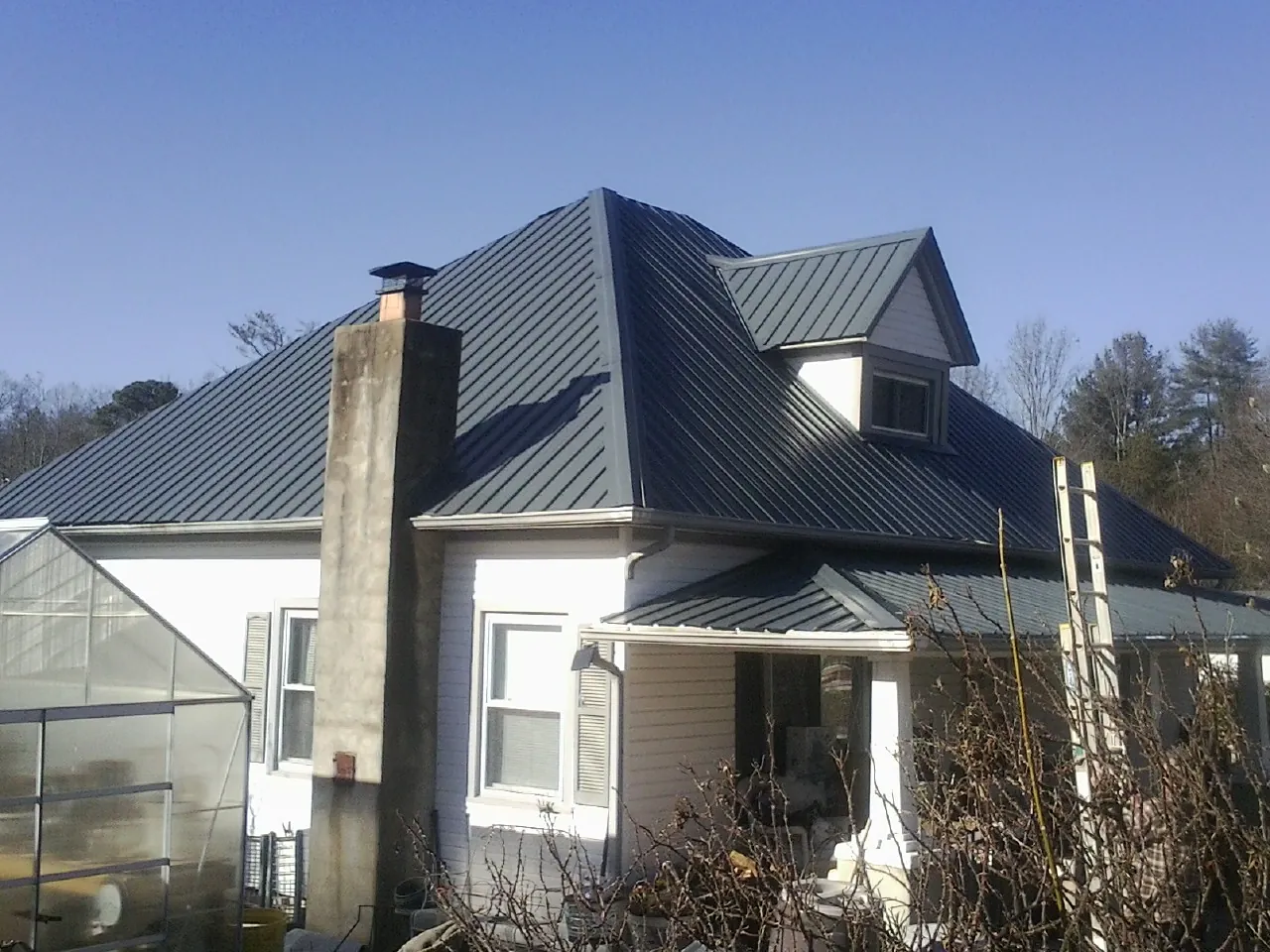 Dark blue standing seam metal roof on a white farmhouse with dormer — Slate & Tile Roof Repair by Roofing Brothers in Lillington