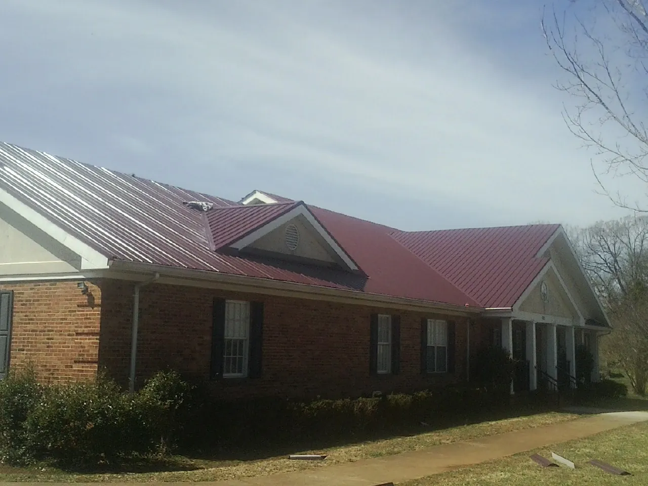 Red metal roof with gabled entries on a long brick building, from a Hail Damage Roof Repair job in Lillington