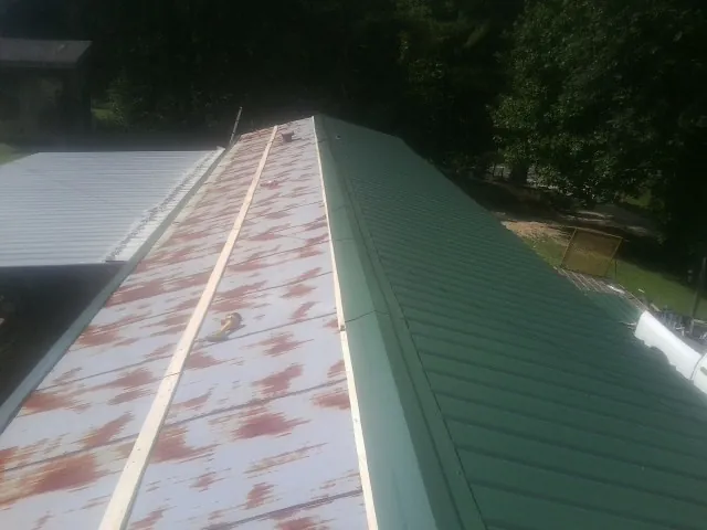 Old rusted panels beside newly installed green metal roofing — Wind Damage Roof Repair by Roofing Brothers in Lillington