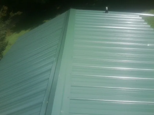 New green metal panels meeting at the ridge of a roof — Flat Roof Repair work by our crew in Lillington