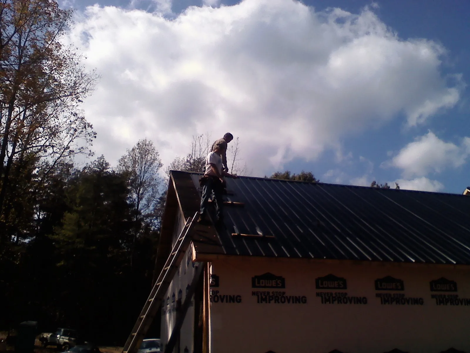 Roofer fastening dark metal panels high against a cloudy sky, from a Roof Inspection job in Lillington