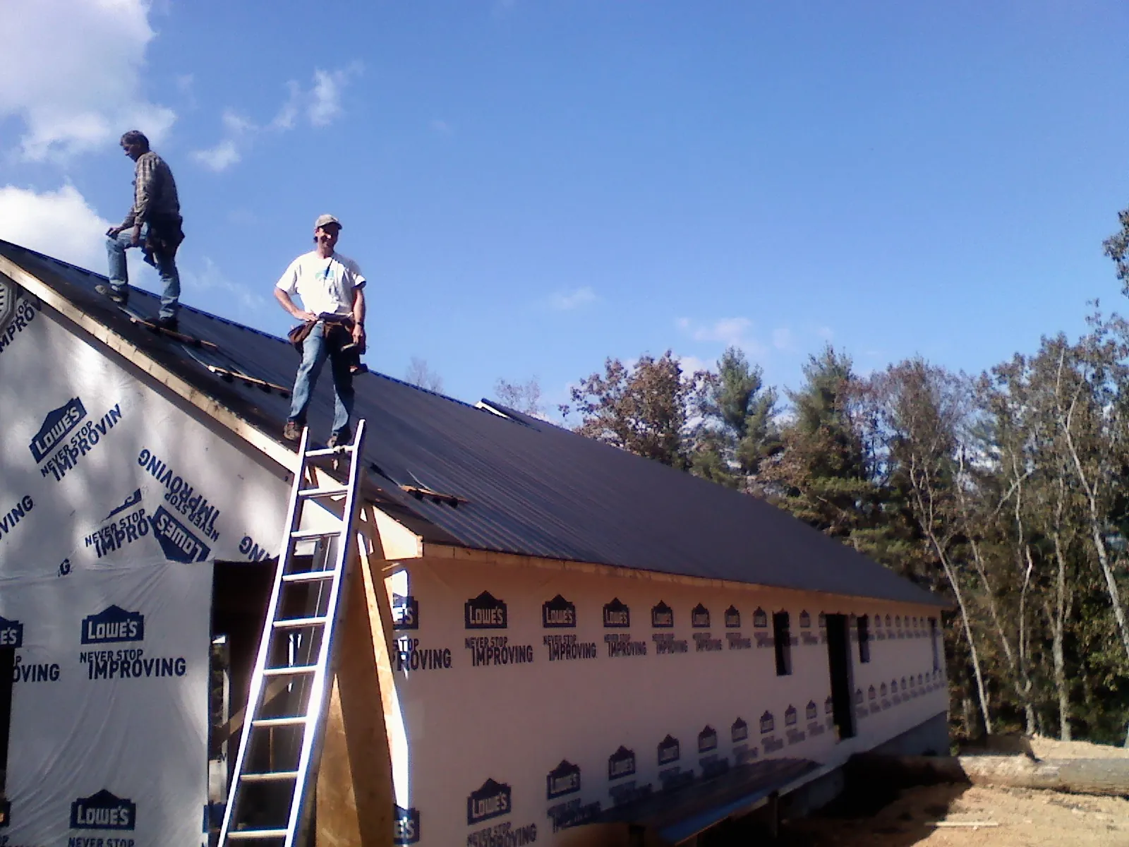 Two roofers standing on a long dark metal roof over a wrapped building in Lillington