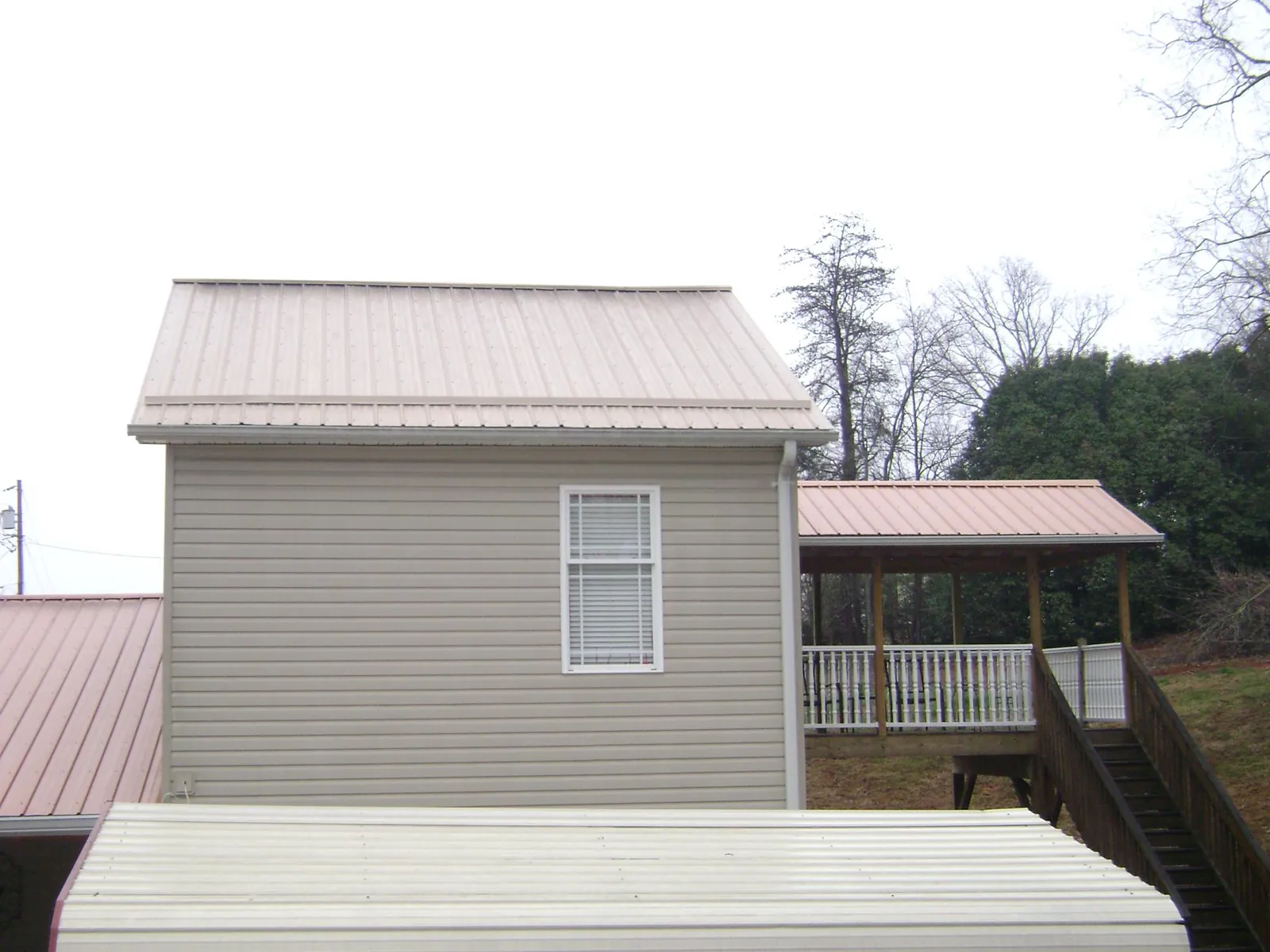 Tan metal roofs on a two story addition and attached porch, from a Roof Replacement job in Lillington